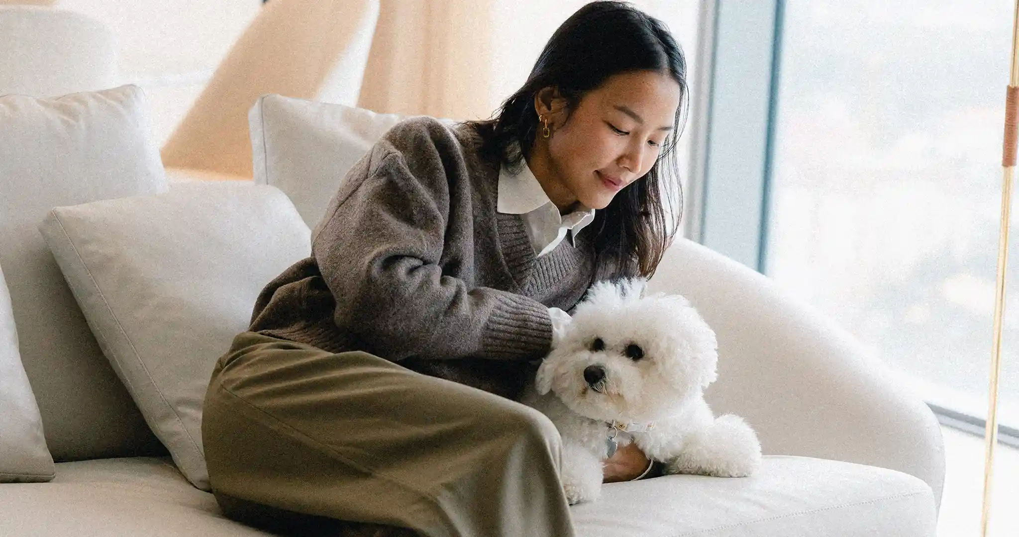 ผู้หญิงนั่งลูบสุนัขสีเขียวที่นอนอยู่บนโซฟาของคอนโดเลี้ยงสัตว์ได้สุขุมวิท